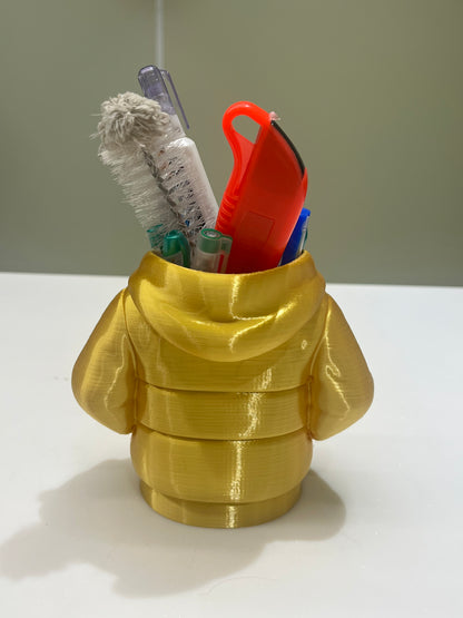 The Mini Hoodie Desk Organizer is a yellow, 3D-printed pen holder shaped like a puffy jacket, storing pens, a utility knife, toothbrush, and cleaning brush—a creative desk accessory for any workspace.