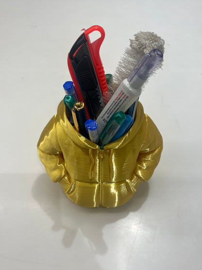 The Mini Hoodie Desk Organizer - 3D Printed Pen Holder is a gold hoodie-shaped desk accessory with hand-in-pocket design, displayed on a white surface and filled with pens, markers, a box cutter, and a cleaning brush.