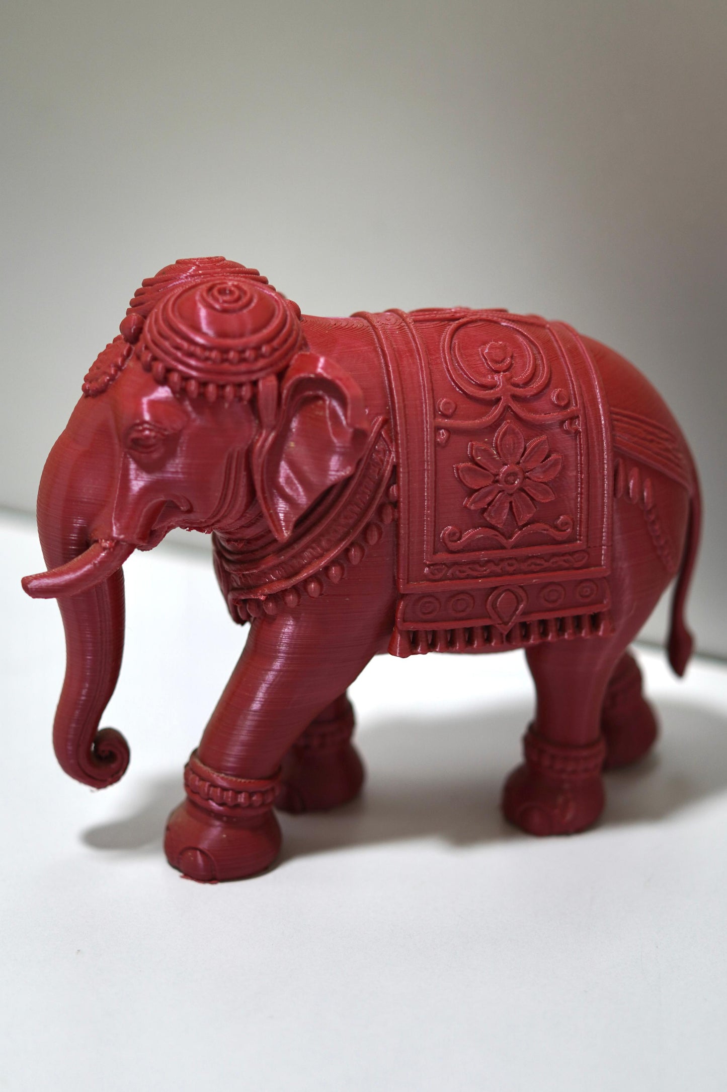 The Royal Prosperity Elephant - 6 Inch features intricate carvings and a rich red finish, standing elegantly on a light surface. This stunning Vastu elephant statue symbolizes prosperity and adds charm to any space.