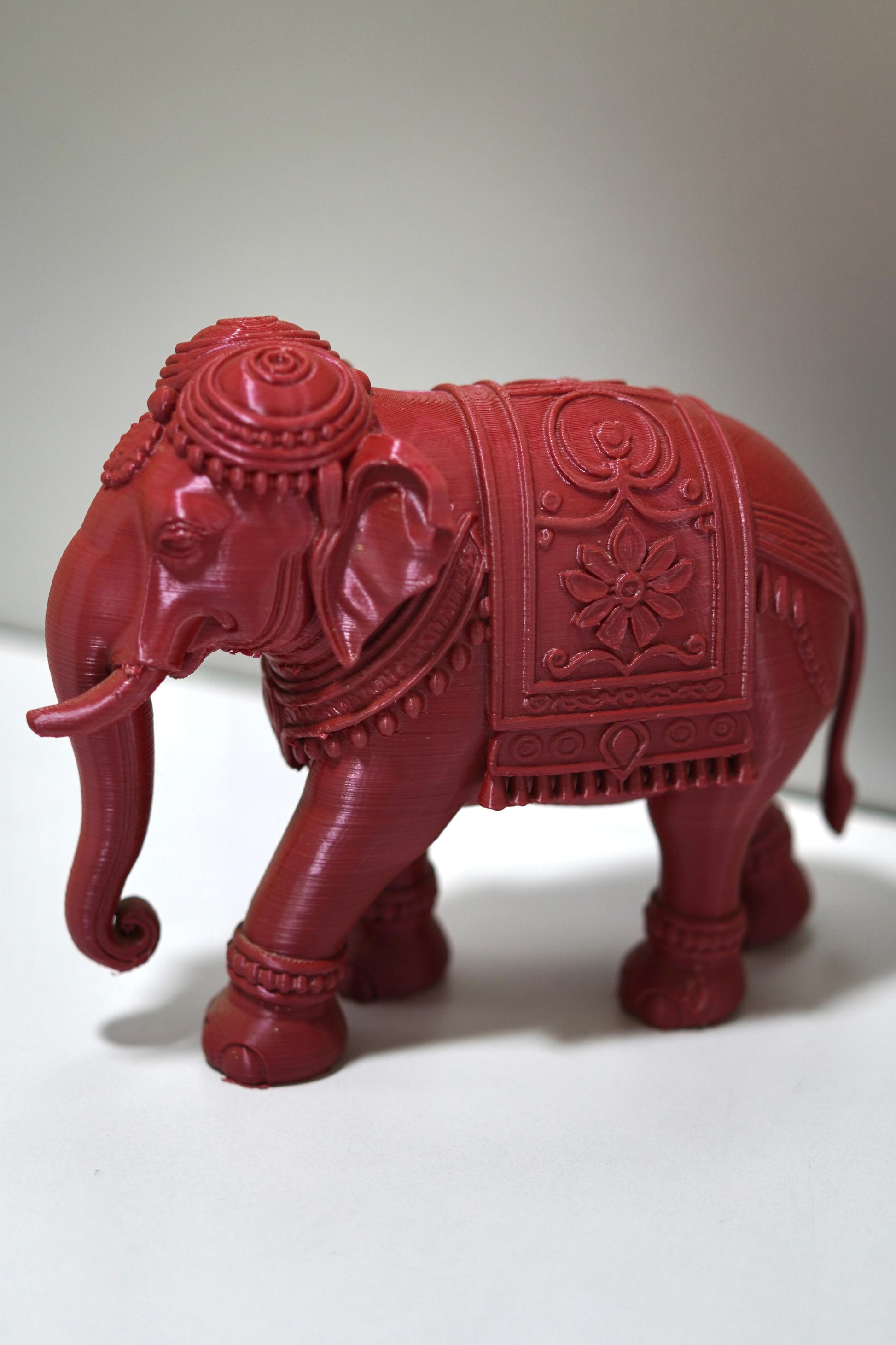 The Royal Prosperity Elephant - 6 Inch features intricate carvings and a rich red finish, standing elegantly on a light surface. This stunning Vastu elephant statue symbolizes prosperity and adds charm to any space.